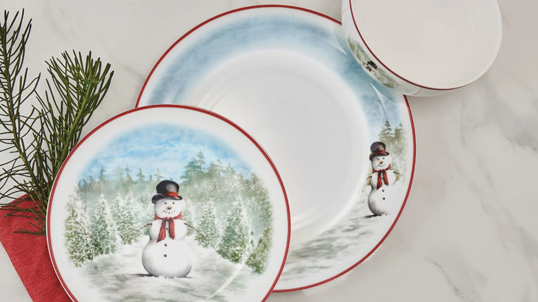 A set of plates and a bowl showing a snowman with a red scarf and black tophat standing in a winter scene.