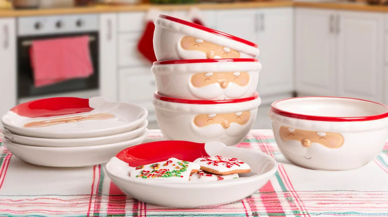 A stack of bowls and plates with Santa faces sitting atop a festive tablecloth.