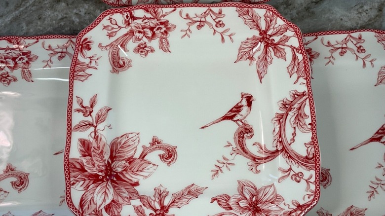 A set of plates and a bowl from a festive dinner set, featuring cardinals and poinsettias on ivory plates.
