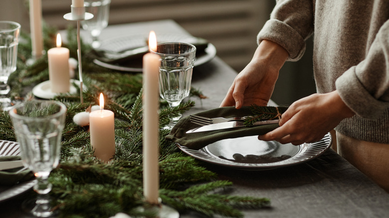 A woman sets cutlery on a dark plate atop a festive table.