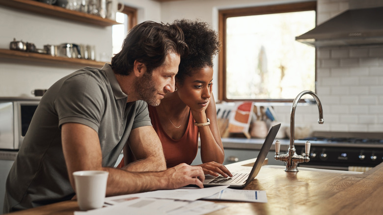 Young couple browsing laptop on wood countertop near kitchen sink