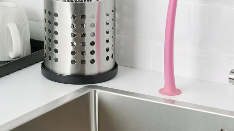 Stainless steel utensil holder with silverware and black tray bottom on white countertop