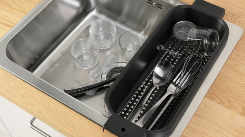 Black IKEA colander repurposed as dish drainer in dirty stainless steel sink