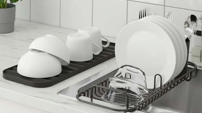 Black IKEA dish rack set stocked with clean white plates, bowls, and mugs in white kitchen
