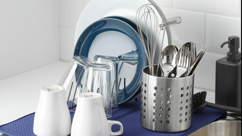 Stainless steel restaurant-style utensil holder with silverware and small cooking utensils beside sink with drying dishes