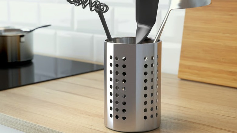 Tall stainless steel cooking utensil holder with clean utensils on wood kitchen countertop