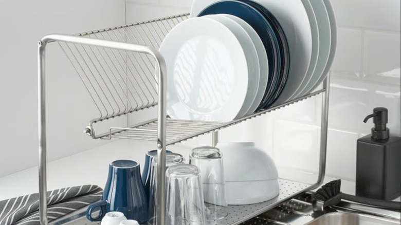 Metal IKEA dish rack with clean plates, bowls, and cups beside stainless steel sink