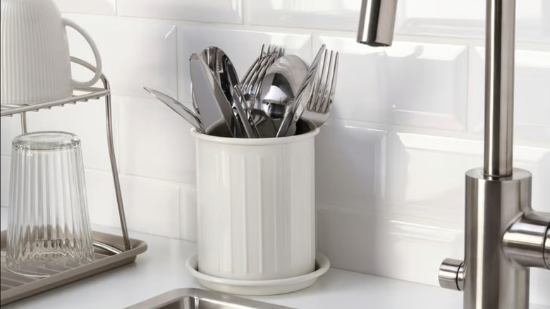 White IKEA cutlery cup with stainless steel silverware by dish rack and sink