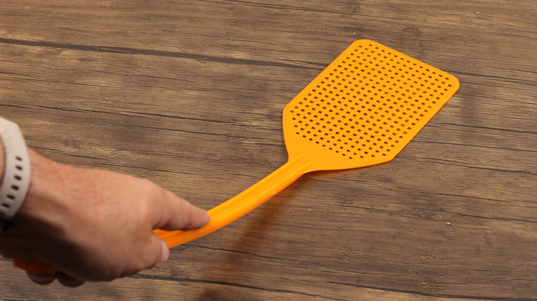 A hand holding a basic, orange fly swatter