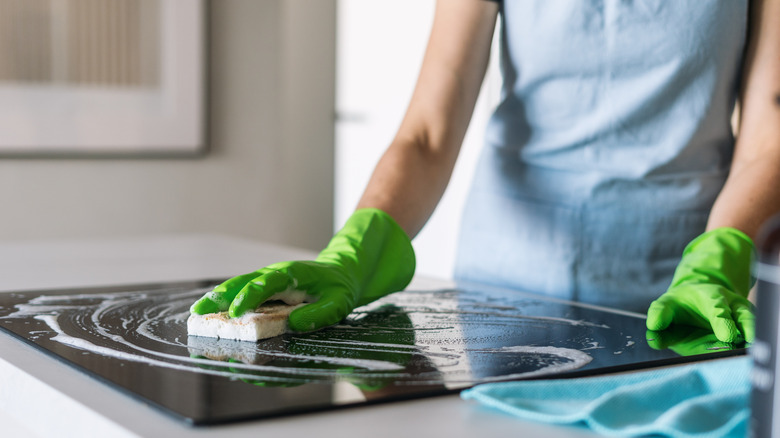Woman wearing green gloves cleaning stovetop with magic eraser