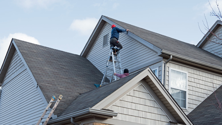Person on ladder on top of roof of a house doing repairs