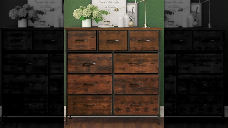 The brown Bigleap 9 Drawer Dresser against a green wall with white decor items on top.