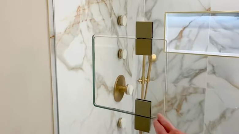 A cut-out in a glass shower door in front of the gold shower knobs