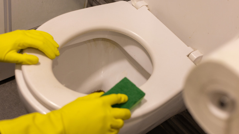 A hand with yellow gloves scrubbing stained toilet