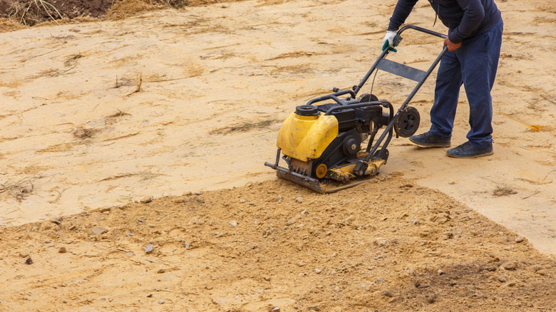 A worker using a soil compactor machine to ram down soil