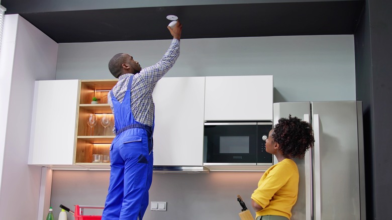 homeowner watches as handyman installs smoke alarm in kitchen