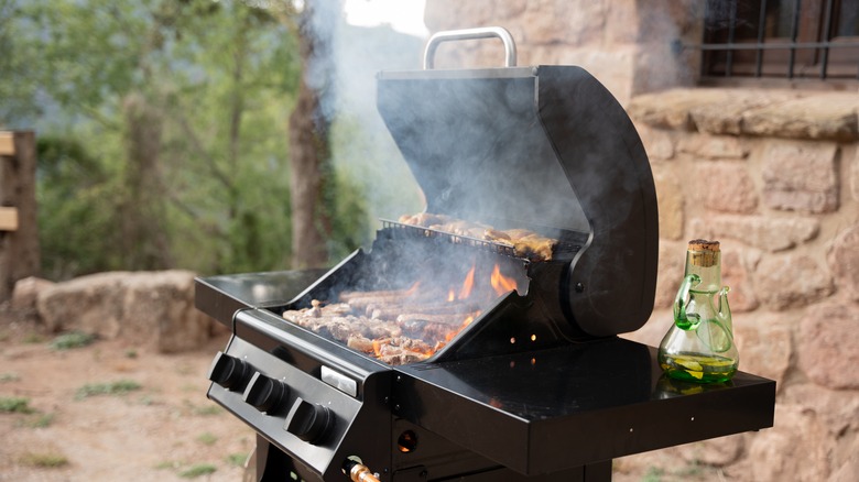 An outdoor grill with food cooking on it, and smoke rising in the air