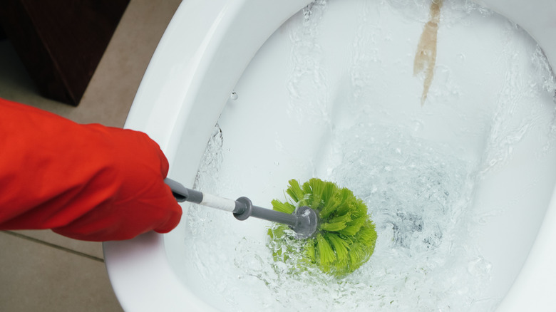 Gloved hand cleaning limescale deposits in a toilet bowl with a brush