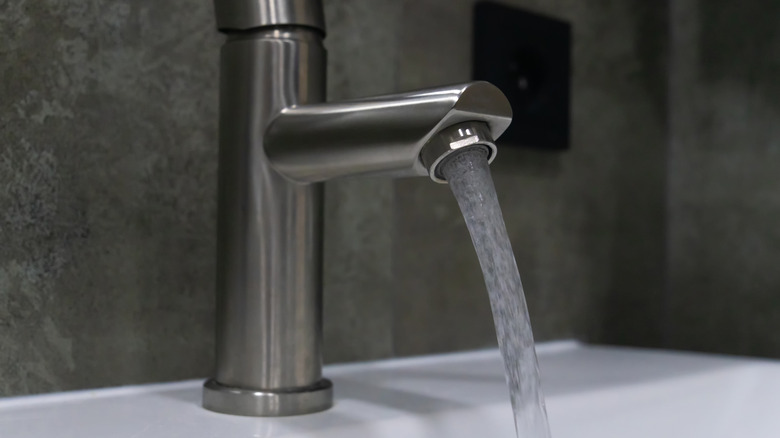 A brushed nickel faucet flowing water into a sink.