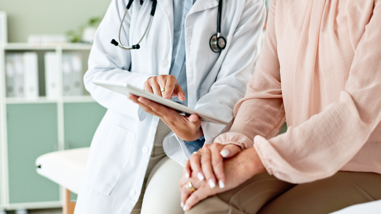 Hands of a doctor showing a patient information on a tablet