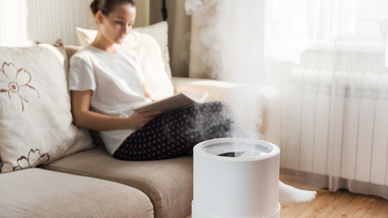 Woman reading on couch in living room with modern humidifier turned on