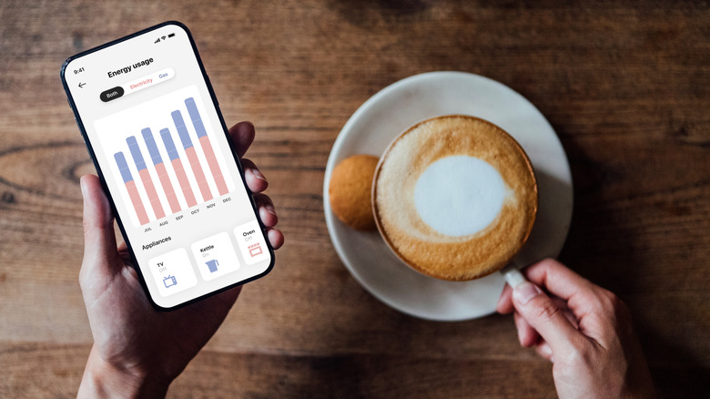 Person monitoring energy usage on phone while enjoying a coffee