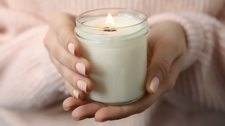 Hands holding white glass candle