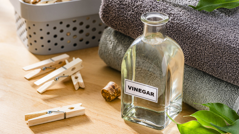 A glass jar labeled as vinegar sits next to a pile of clean towels and some clothespins