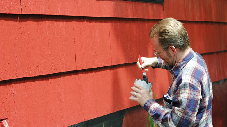 A man painting the exterior of a house red
