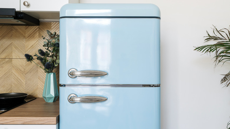 A retro-style blue refrigerator stands against a white wall and cabinets with wooden countertops.