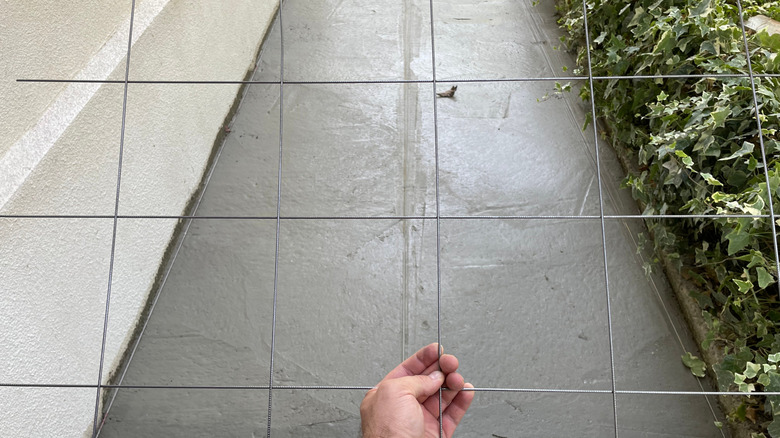 A hand holding the remainder of a sheet of welded wire mesh that was used to reinforce a concrete walkway