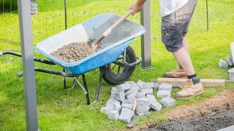 A person using a shovel to remove aggregate from a wheelbarrow while building a walkway