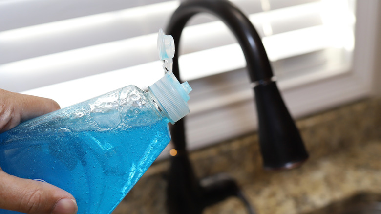 A person holding bottle of blue dish soap
