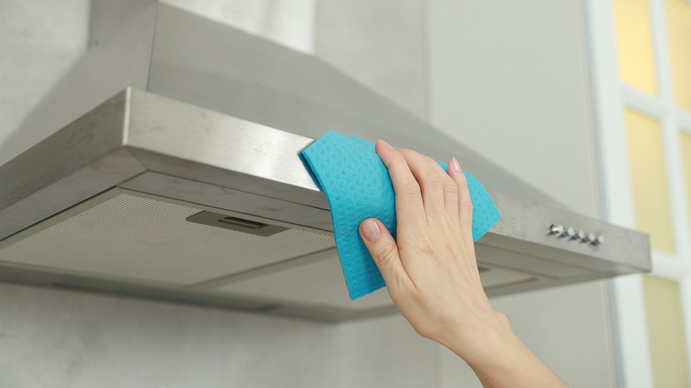 A woman using a cloth to wipe down a range hood