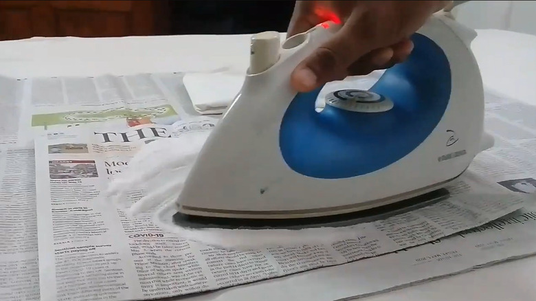 Someone cleaning burnt iron soleplate by rubbing it over salt spread on newspaper