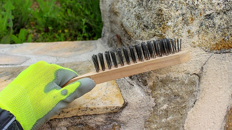 A person using a stiff brush to clean a stone retaining wall