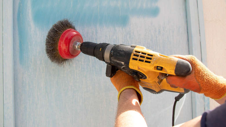 Close-up of person using wire brush drill attachment on a painted blue wall