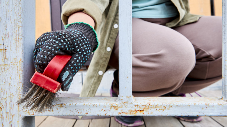 Someone using a stiff wire brush to clean off rust from a house