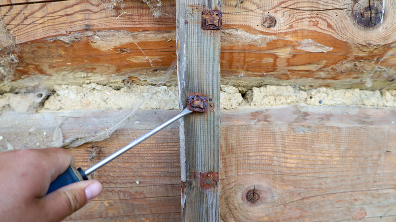 A hand with a tool trying to undo a rusty bolt on the side of a house