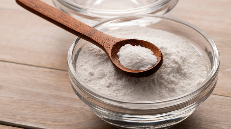 Baking soda in a glass bowl on a wooden countertop with a wooden spoon.