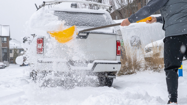 A person removes snow from their driveway using a yellow snow shovel.
