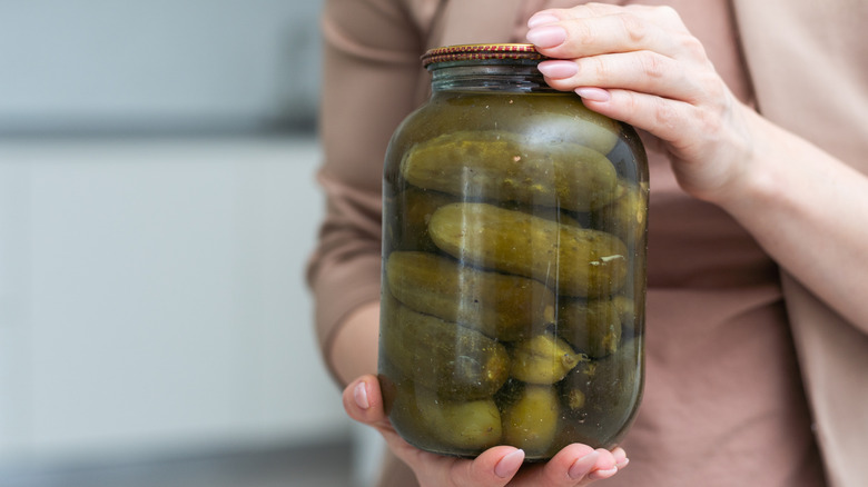 A woman holds a jar of pickles.