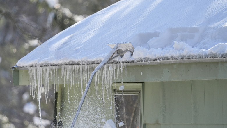 Roof raking brushing snow off of a roof overhang