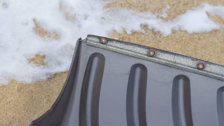 Black snow shovel with a worn metal edge with snowy concrete in the background