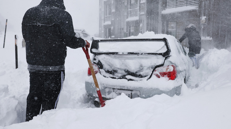People shoveling deep snow around a car