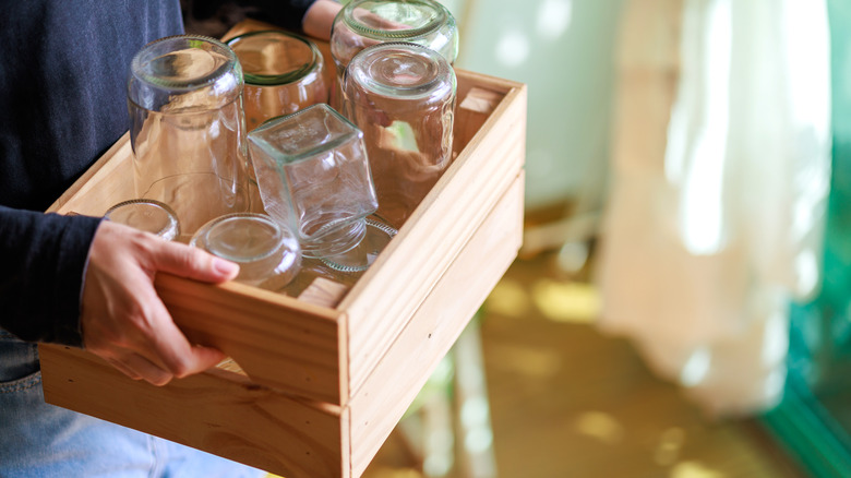 Person in blue sweater carrying wood crate full of glass jars
