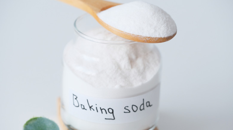 a glass jar labeled 'baking soda' in hand written letters and a wooden spoon holding some of the poweder