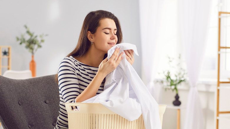 Woman sitting in a chair smiling while smelling clean laundry with a basket on her lap.