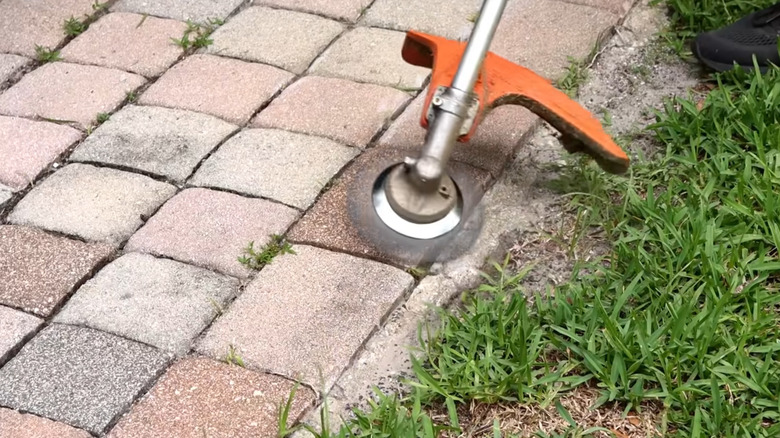 A contractor using the wire wheel brush attachment to clear weeds from the curb