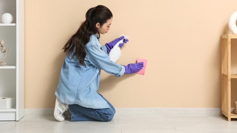 Woman cleaning wall with spray solution and sponge